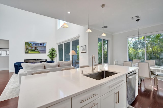 kitchen with sink, dishwasher, hanging light fixtures, white cabinets, and a center island with sink