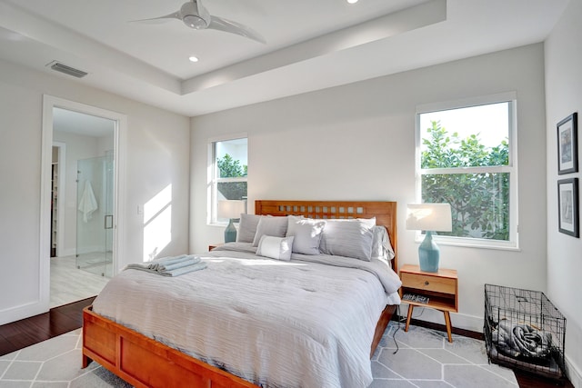 bedroom with ensuite bath, light hardwood / wood-style flooring, a raised ceiling, and ceiling fan