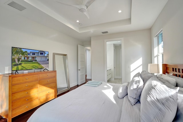 bedroom with dark hardwood / wood-style flooring, a tray ceiling, ensuite bath, and ceiling fan