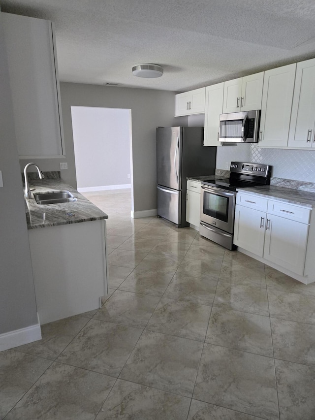 kitchen with appliances with stainless steel finishes, sink, white cabinets, dark stone counters, and a textured ceiling