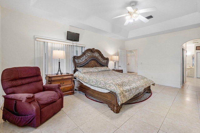 bedroom featuring ceiling fan, connected bathroom, a tray ceiling, and light tile patterned floors