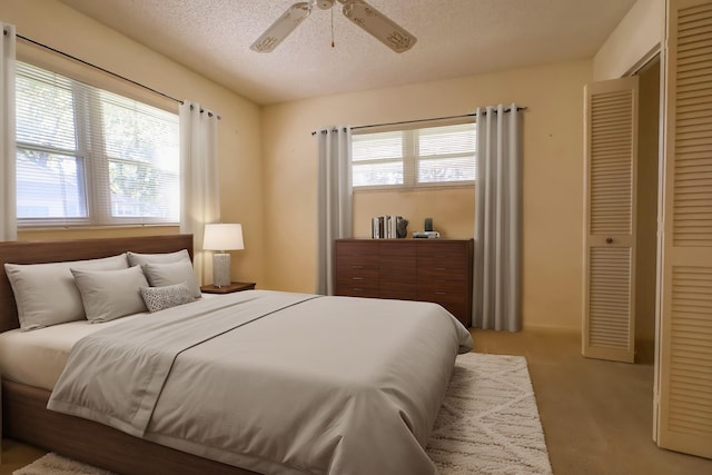 carpeted bedroom with ceiling fan, a closet, multiple windows, and a textured ceiling