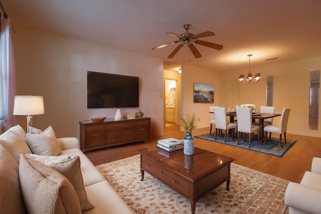 living room featuring hardwood / wood-style flooring, ceiling fan with notable chandelier, and a textured ceiling