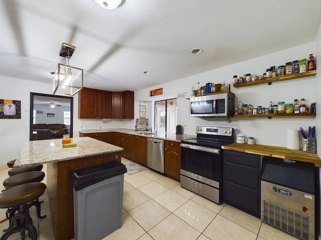 kitchen with sink, light tile patterned floors, stainless steel appliances, a kitchen island, and decorative light fixtures