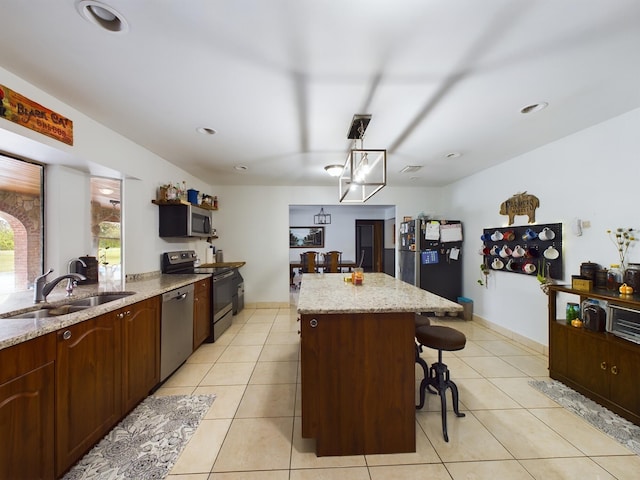 kitchen with sink, light tile patterned floors, hanging light fixtures, stainless steel appliances, and a kitchen island