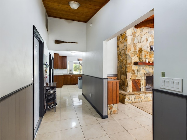 kitchen featuring light tile patterned floors, wood ceiling, a stone fireplace, and a towering ceiling