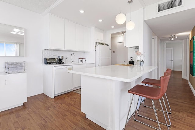 kitchen with visible vents, a kitchen breakfast bar, backsplash, white appliances, and a peninsula