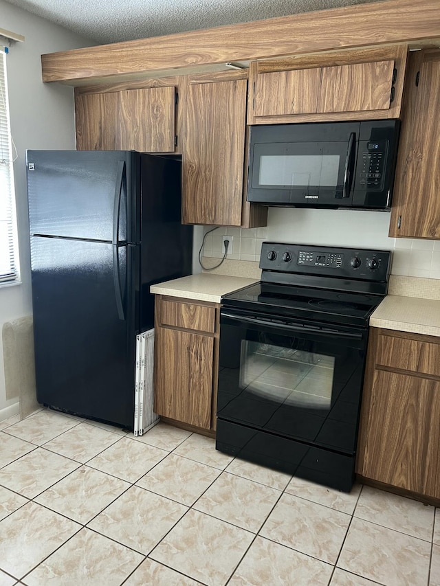 kitchen with light tile patterned floors, a textured ceiling, and black appliances