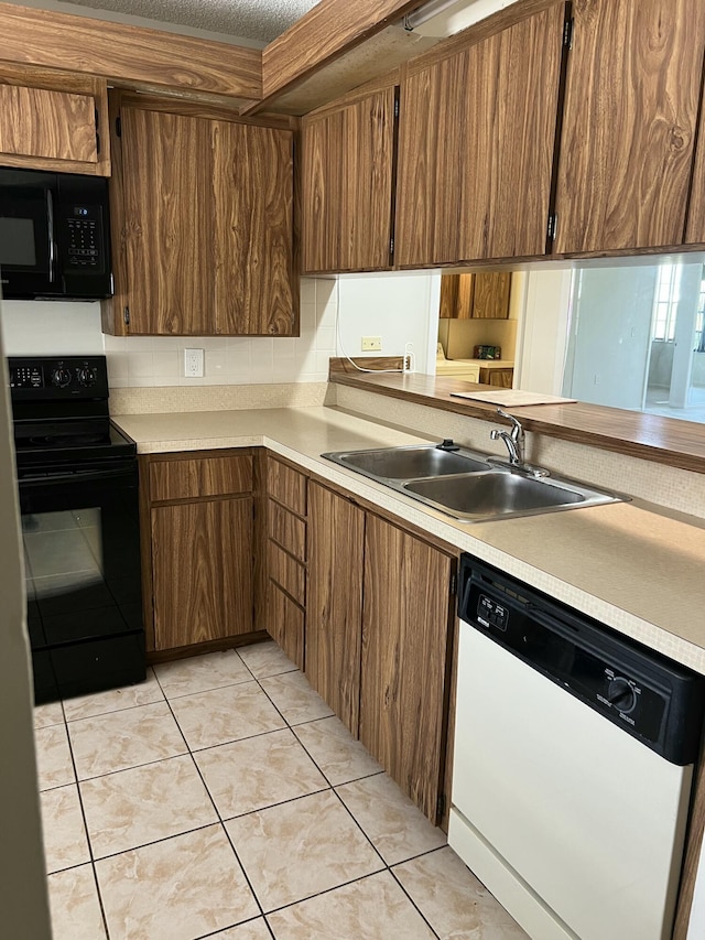 kitchen featuring sink, light tile patterned floors, tasteful backsplash, black appliances, and kitchen peninsula