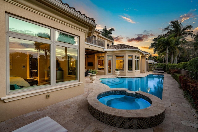 pool at dusk featuring an in ground hot tub and a patio area