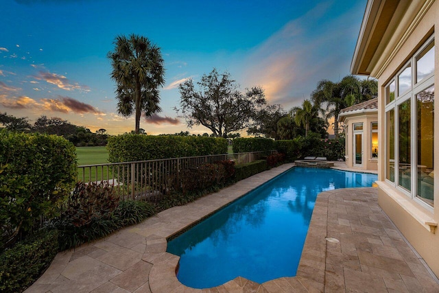 pool at dusk with a patio and an in ground hot tub