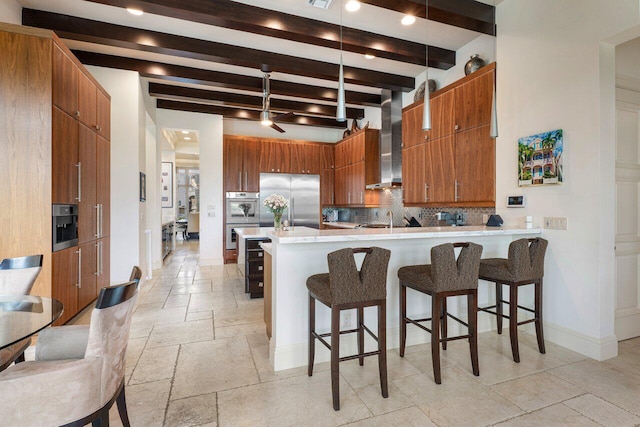 kitchen featuring appliances with stainless steel finishes, a kitchen breakfast bar, kitchen peninsula, and wall chimney range hood