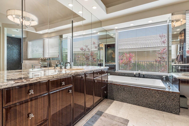 bathroom featuring a raised ceiling, vanity, a relaxing tiled tub, and tile patterned floors