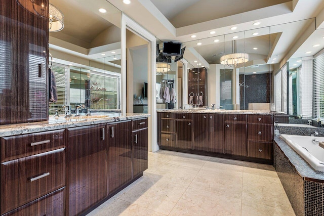 bathroom with vaulted ceiling, tile patterned flooring, vanity, a tray ceiling, and tiled tub