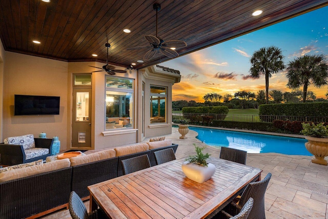 pool at dusk with a patio area, outdoor lounge area, and ceiling fan