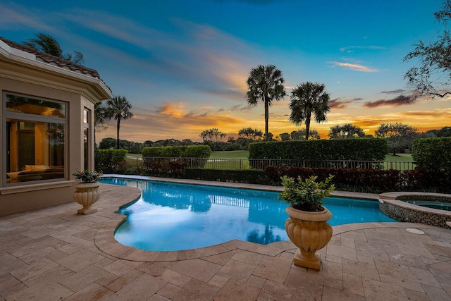 pool at dusk with a patio area and an in ground hot tub