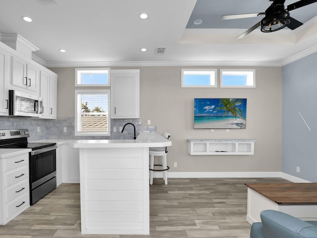 kitchen with crown molding, a breakfast bar, white cabinetry, backsplash, and stainless steel appliances