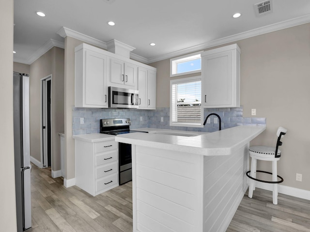 kitchen with white cabinetry, a kitchen breakfast bar, kitchen peninsula, stainless steel appliances, and backsplash