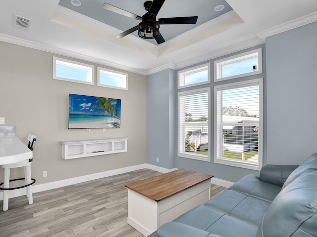 living room featuring ceiling fan, ornamental molding, a raised ceiling, and light hardwood / wood-style floors