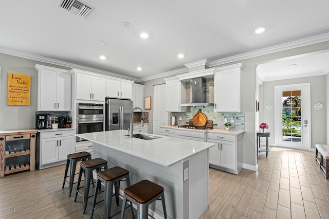 kitchen with sink, white cabinetry, appliances with stainless steel finishes, a kitchen breakfast bar, and wall chimney range hood