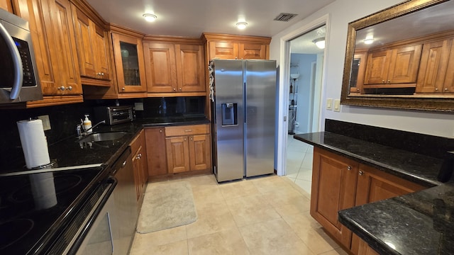 kitchen with light tile patterned flooring, sink, tasteful backsplash, dark stone counters, and stainless steel appliances