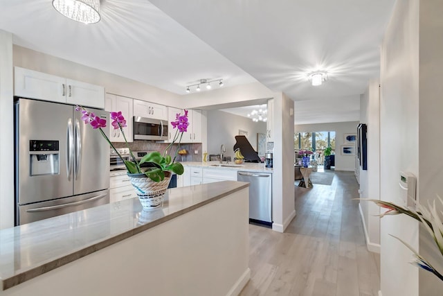 kitchen with white cabinetry, stainless steel appliances, a notable chandelier, light hardwood / wood-style floors, and light stone countertops