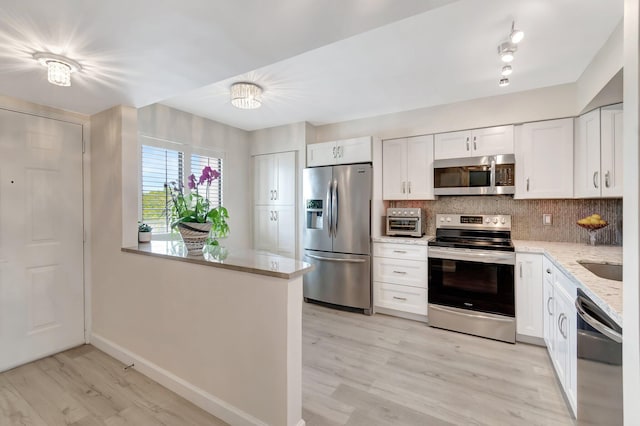 kitchen with stainless steel appliances, tasteful backsplash, light stone countertops, light hardwood / wood-style floors, and white cabinets