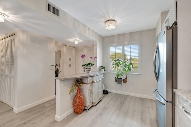 kitchen featuring white cabinetry, light stone countertops, stainless steel refrigerator, and light hardwood / wood-style floors