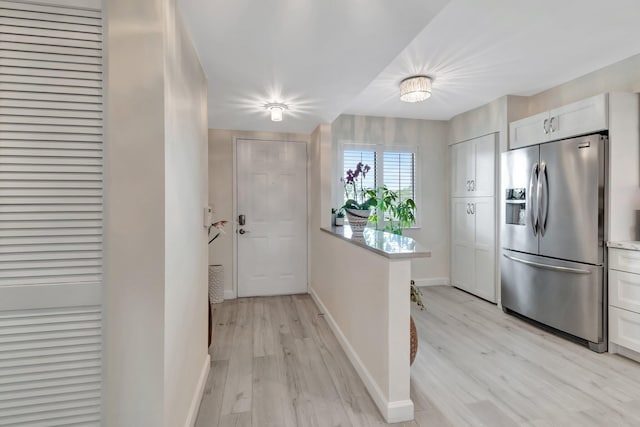 kitchen with stainless steel refrigerator with ice dispenser, white cabinets, and light hardwood / wood-style flooring