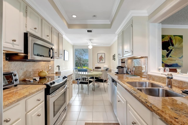 kitchen featuring sink, appliances with stainless steel finishes, a tray ceiling, light stone countertops, and white cabinets