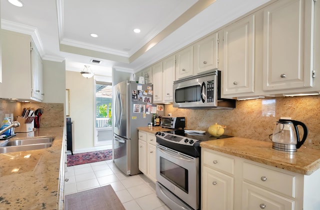 kitchen featuring a raised ceiling, sink, stainless steel appliances, crown molding, and light stone countertops