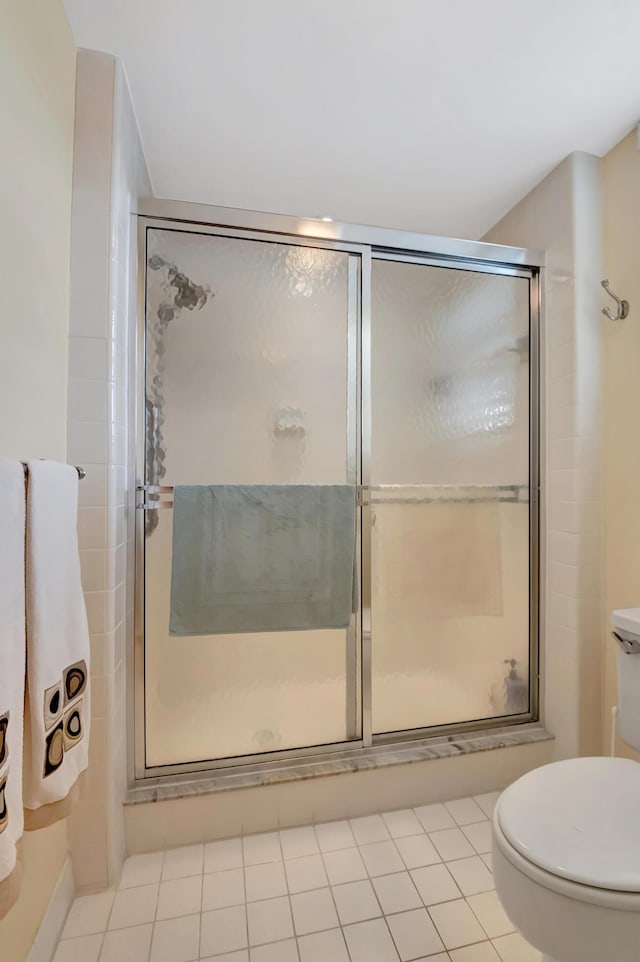 bathroom featuring toilet, a shower with door, and tile patterned flooring