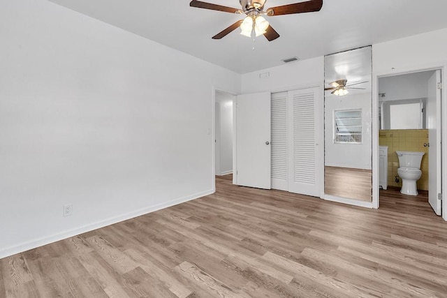 unfurnished bedroom with ensuite bathroom, ceiling fan, light wood-type flooring, and a closet