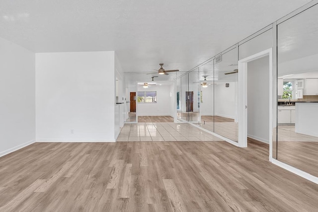 unfurnished living room featuring ceiling fan, sink, and light wood-type flooring