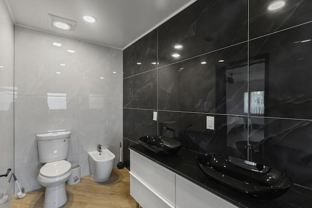 bathroom with wood-type flooring, tile walls, vanity, toilet, and a bidet