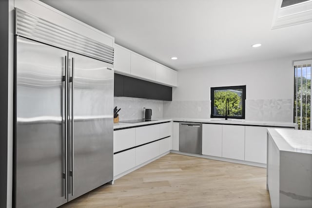 kitchen with sink, appliances with stainless steel finishes, white cabinetry, tasteful backsplash, and light hardwood / wood-style floors