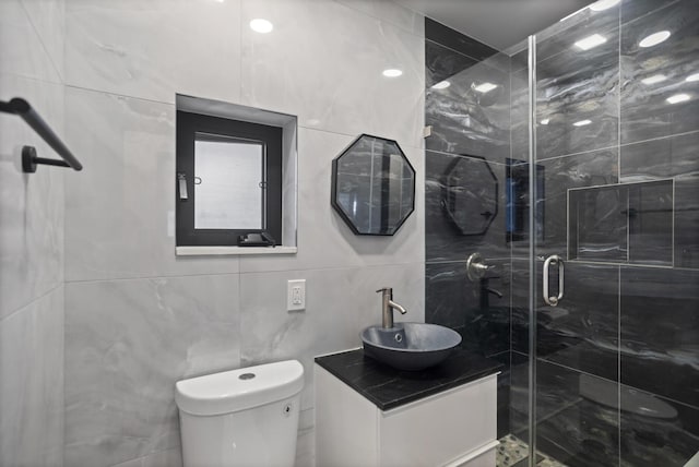 bathroom with a shower with door, vanity, tile walls, and toilet