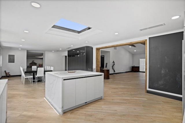 kitchen with white cabinetry, a center island, light hardwood / wood-style floors, and a skylight