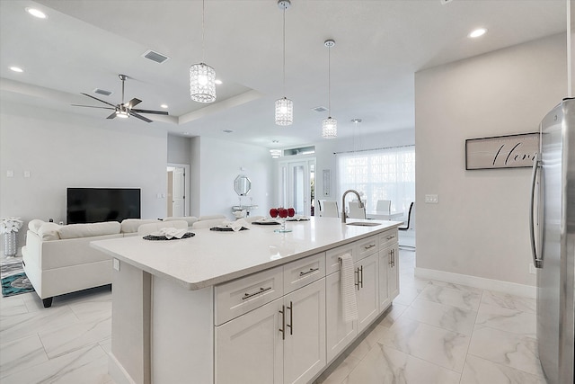 kitchen featuring pendant lighting, sink, stainless steel refrigerator, an island with sink, and white cabinets