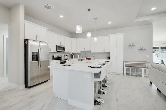 kitchen with pendant lighting, stainless steel appliances, a kitchen island with sink, and white cabinets