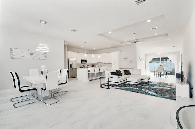 living room featuring a raised ceiling and ceiling fan with notable chandelier