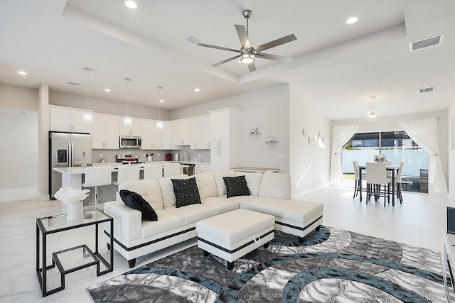 living room with sink, ceiling fan with notable chandelier, and a tray ceiling