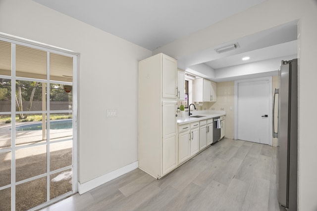 kitchen with sink, appliances with stainless steel finishes, white cabinetry, tasteful backsplash, and light wood-type flooring