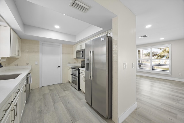 kitchen with stainless steel appliances, white cabinetry, sink, and light wood-type flooring