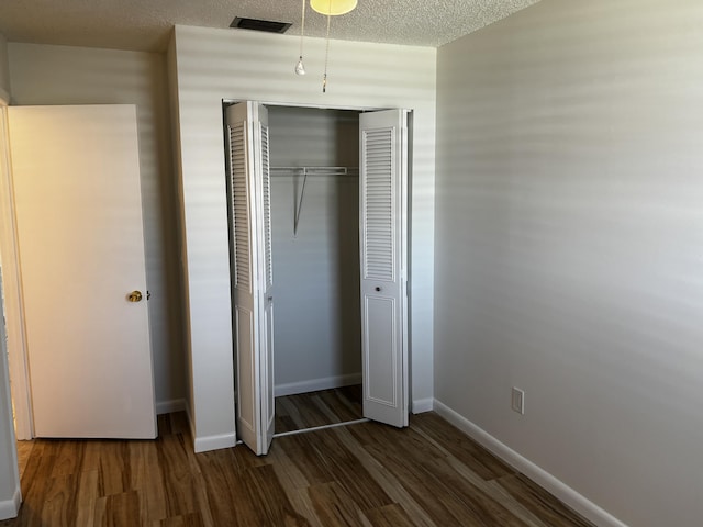 unfurnished bedroom featuring a closet, visible vents, a textured ceiling, wood finished floors, and baseboards