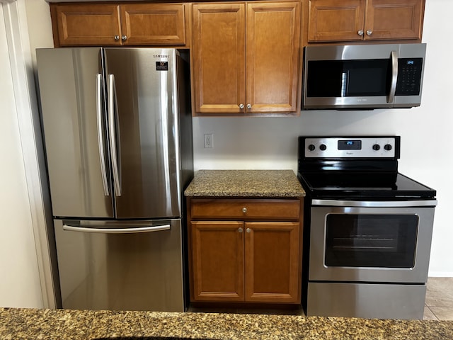 kitchen featuring stainless steel appliances, brown cabinetry, and dark stone countertops