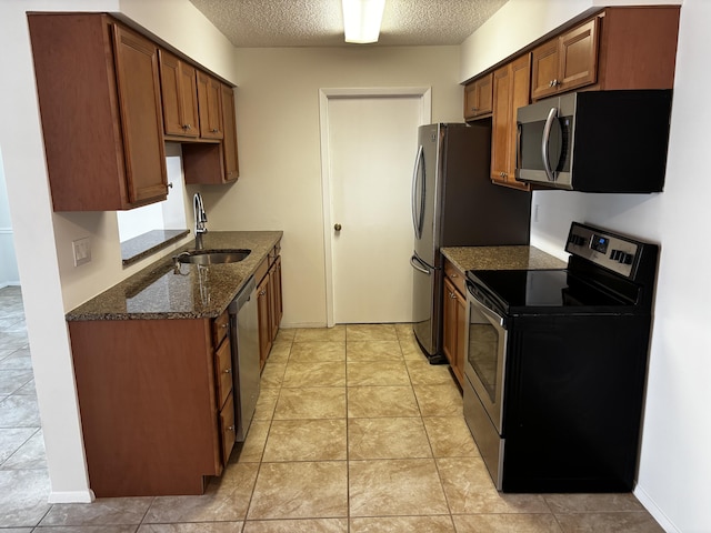 kitchen featuring a textured ceiling, light tile patterned floors, a sink, appliances with stainless steel finishes, and dark stone countertops