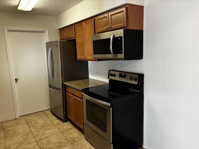 kitchen featuring stainless steel appliances, brown cabinets, a textured ceiling, and light tile patterned floors