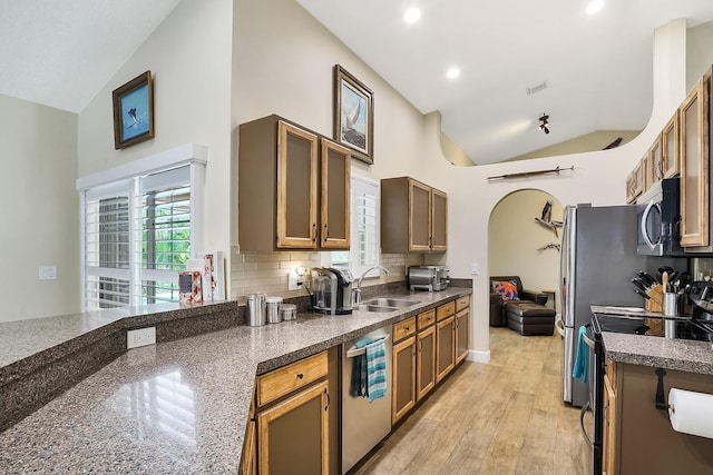 kitchen with sink, light hardwood / wood-style flooring, appliances with stainless steel finishes, high vaulted ceiling, and decorative backsplash