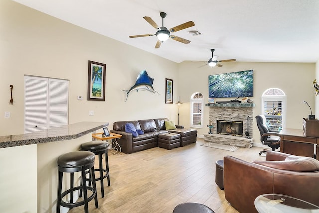 living room featuring ceiling fan, lofted ceiling, a fireplace, and light wood-type flooring